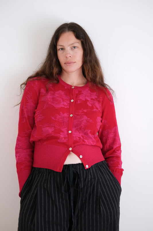 Woman wearing a red patterned cardigan with black pants against a white background