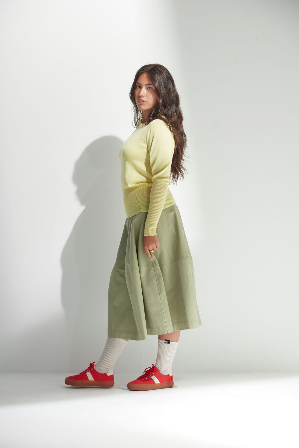 Woman wearing a yellow top and green skirt with red shoes on a white background