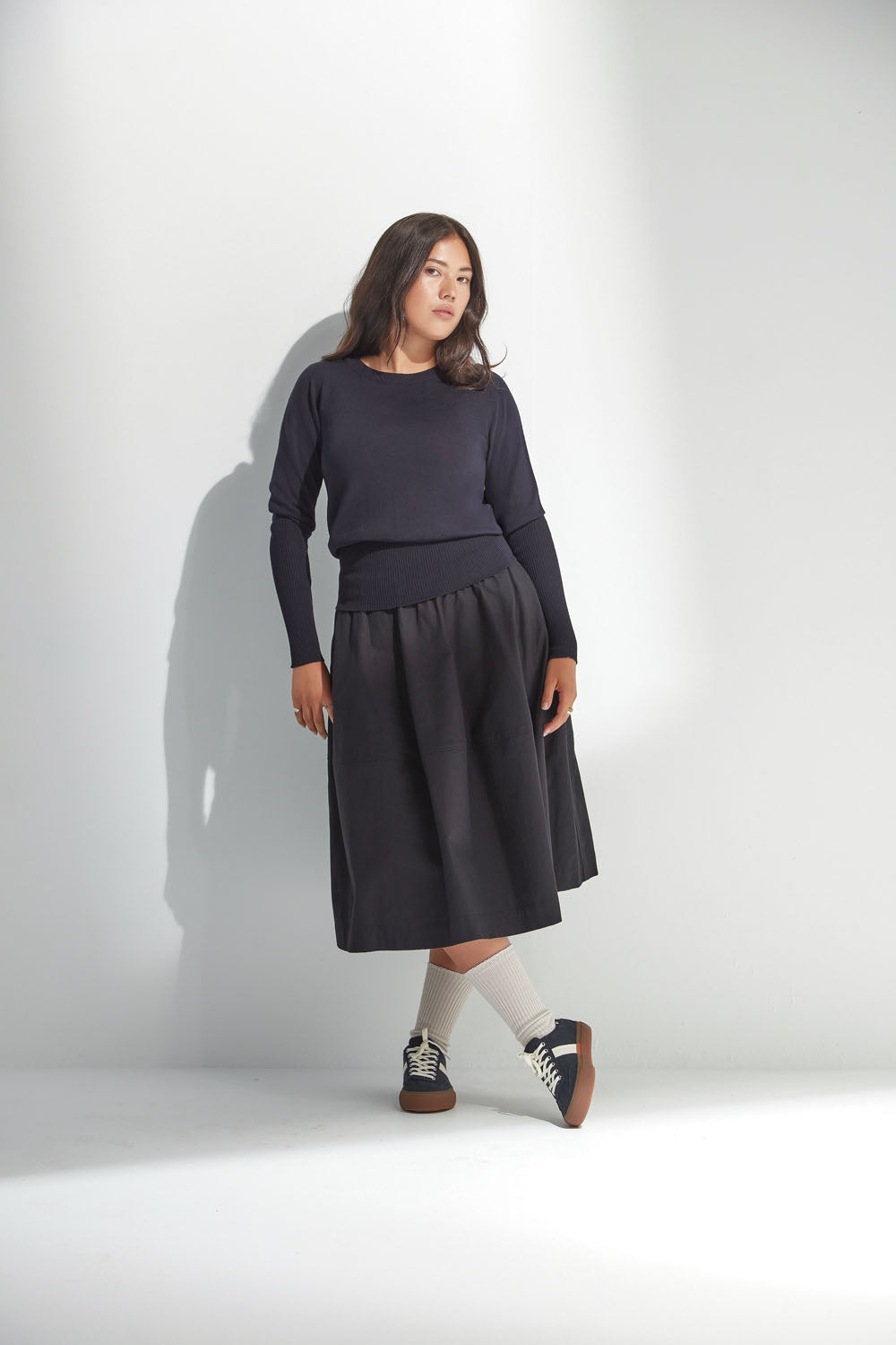 Woman wearing a navy sweater with a black skirt against a white background