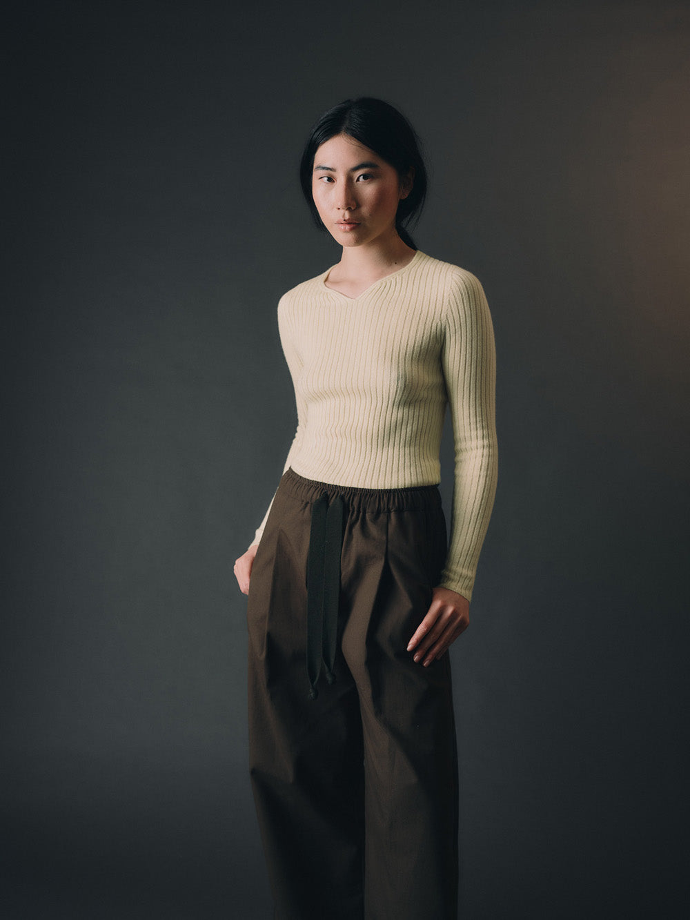 Woman wearing a light yellow cashmere sweater and dark pants against a gray background