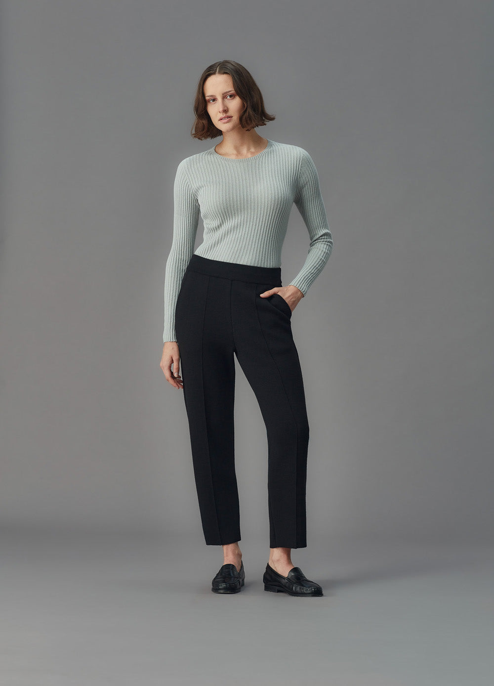 Woman wearing a light blue ribbed top and black pants against a gray background