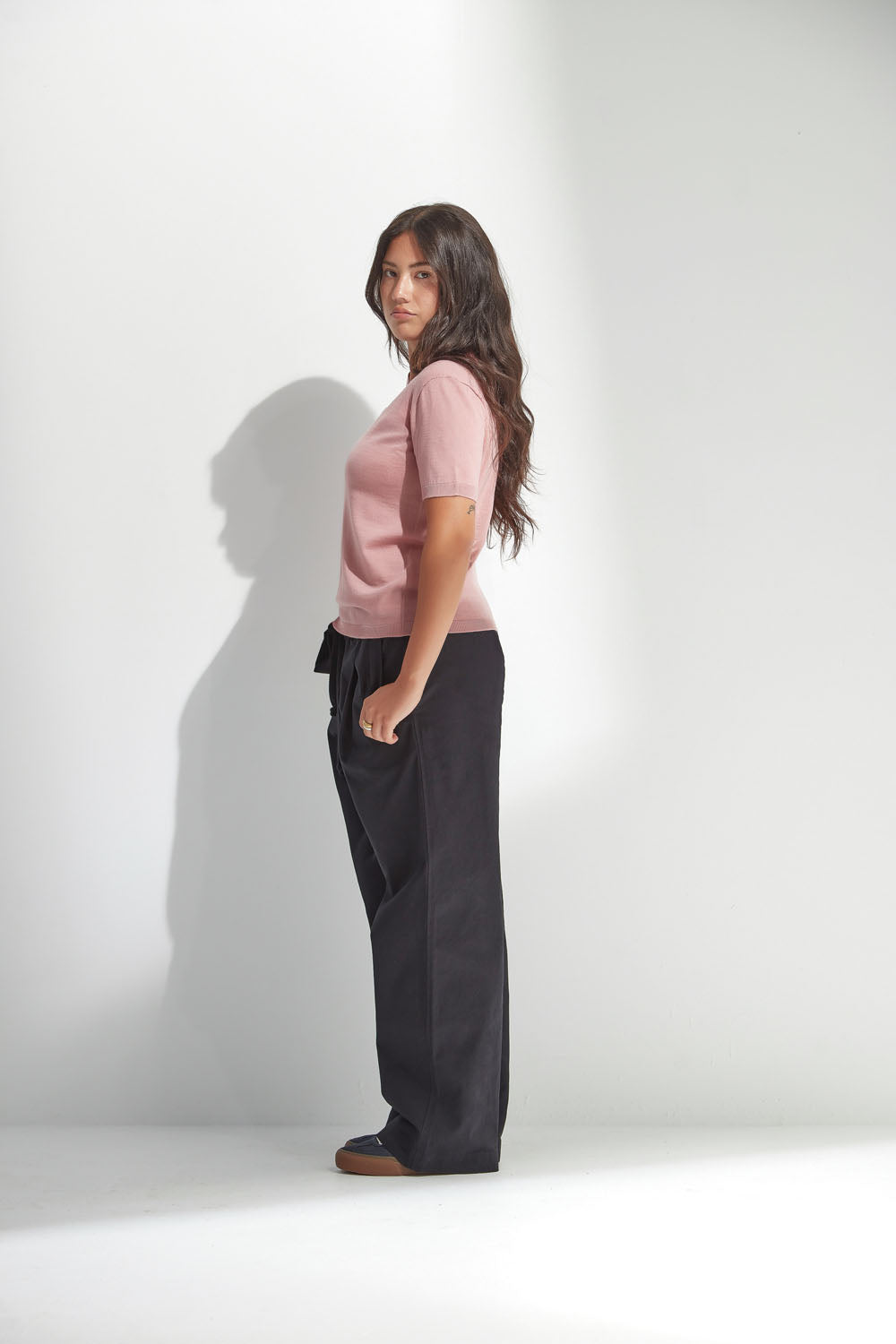 Woman wearing a pink top and black pants against a white background