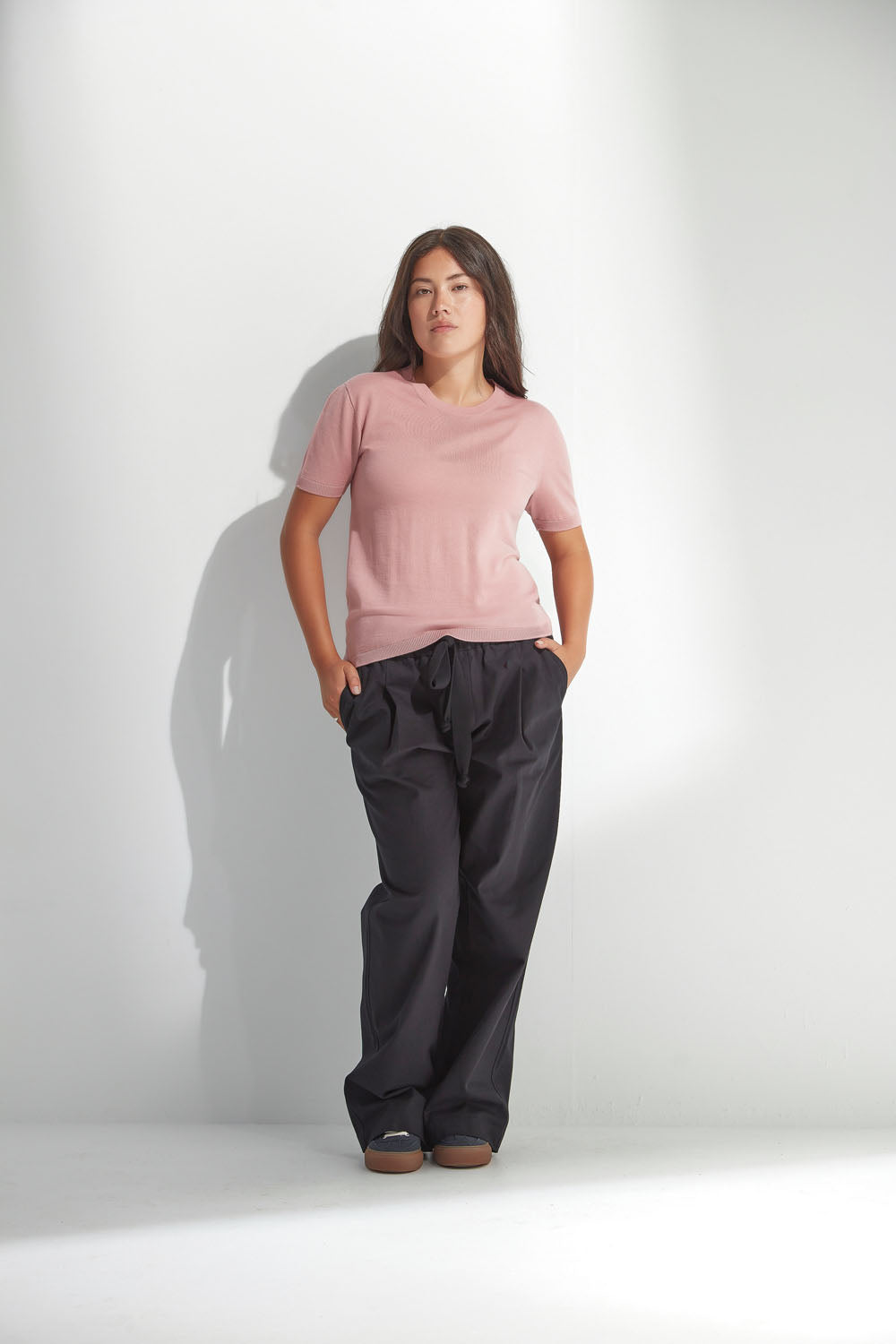 Woman wearing a pink top and dark pants against a white background