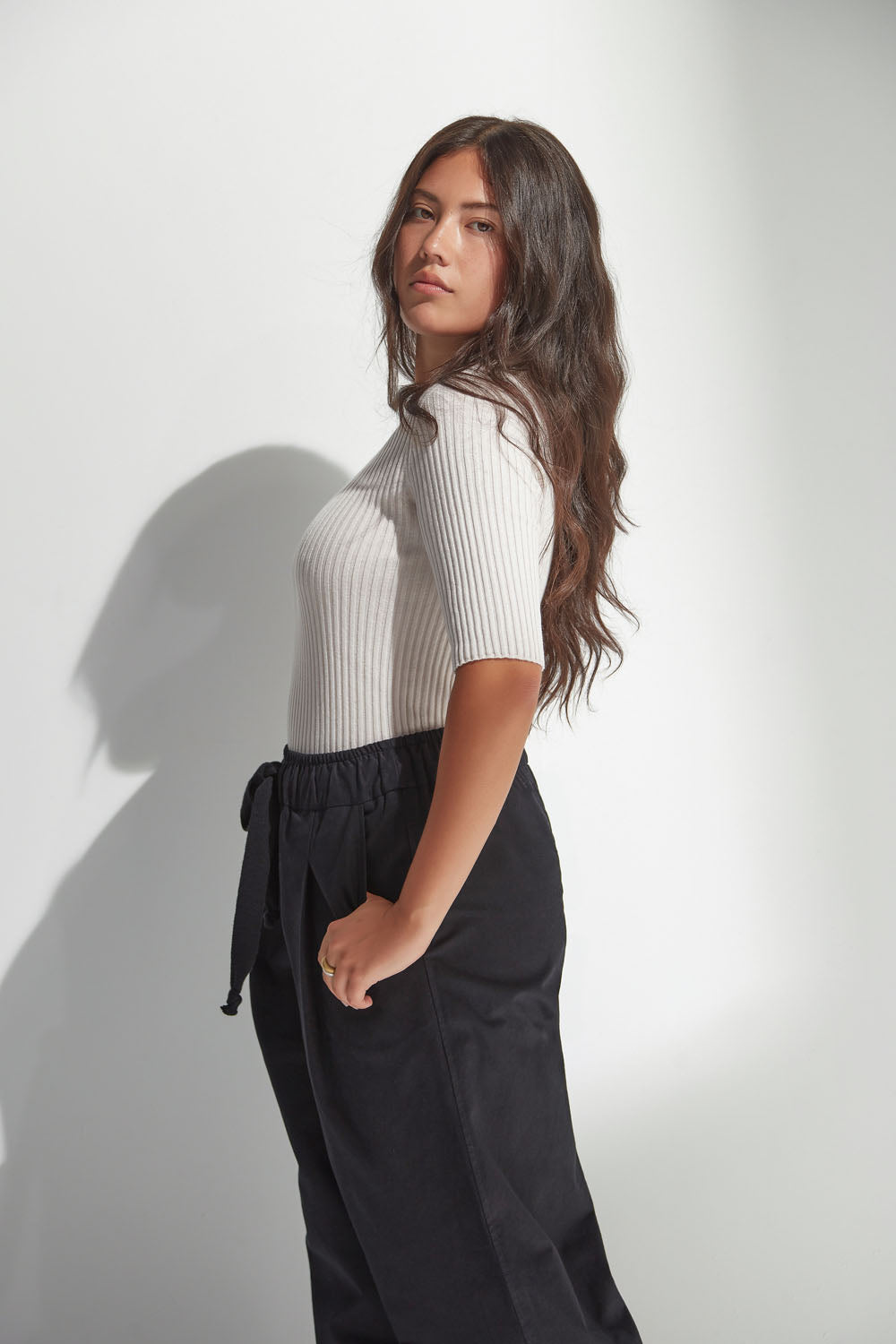 Woman wearing a white ribbed top and black pants against a plain background