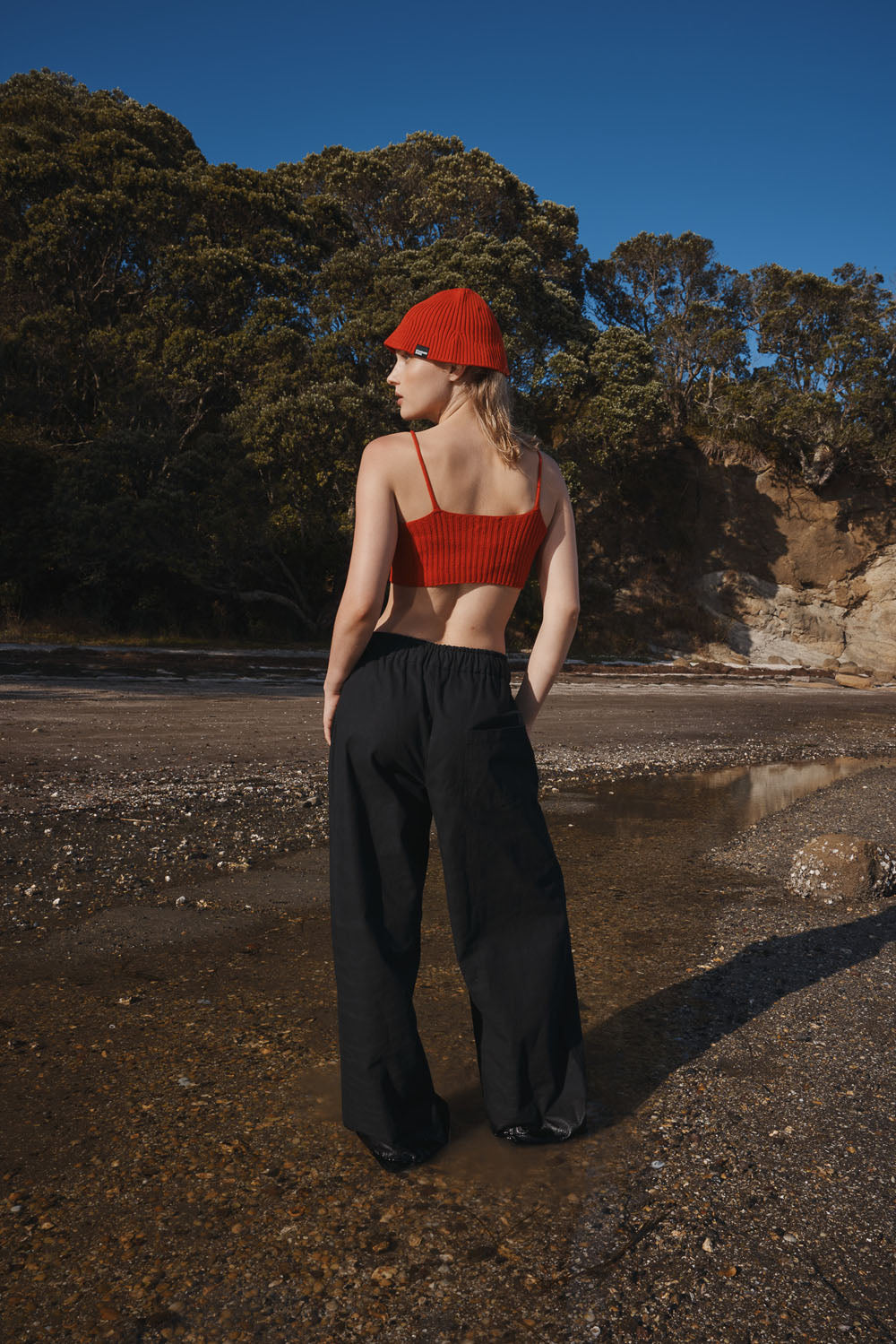 Woman wearing a red top and black pants standing on a beach with trees in the background