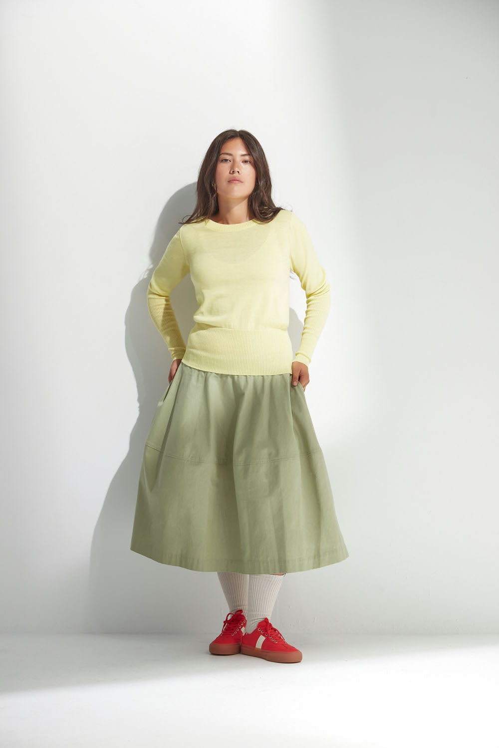 Woman wearing a light yellow sweater and light green skirt on a white background.