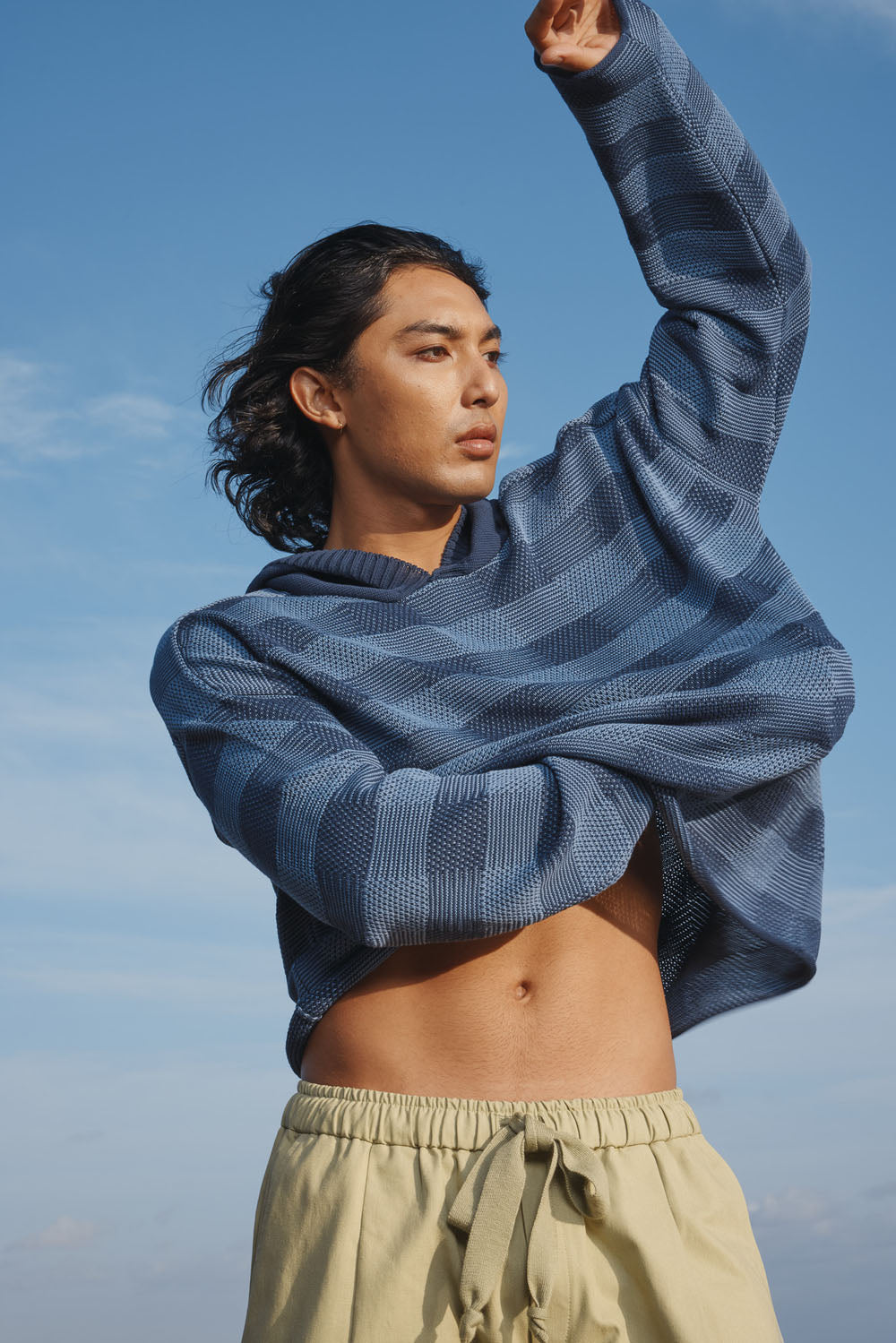 Man wearing a blue checkered sweater and green pants against a clear blue sky.