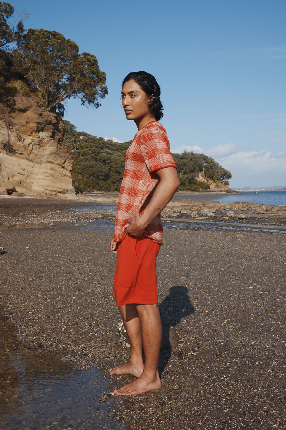 Man standing on a beach wearing a red and white checkered shirt and red shorts.