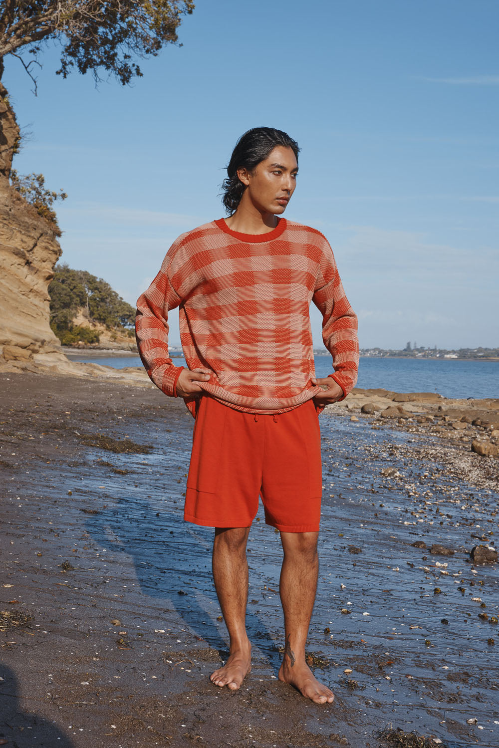 Man wearing a red and white checkered sweater and red shorts standing on a beach.