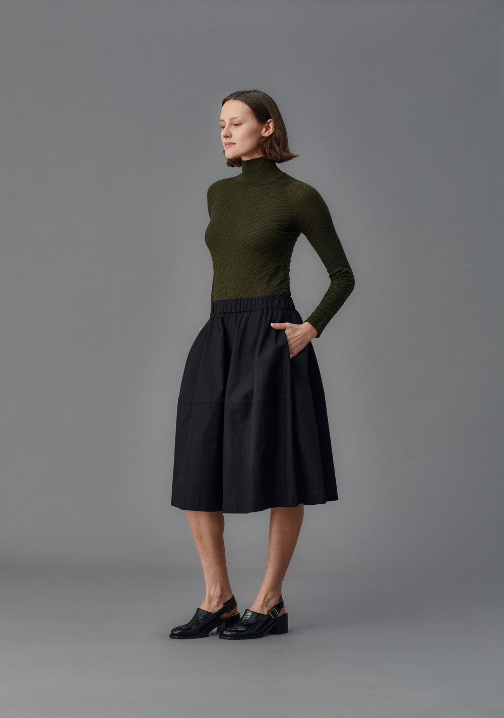 Woman wearing a green turtleneck and black skirt on a gray background