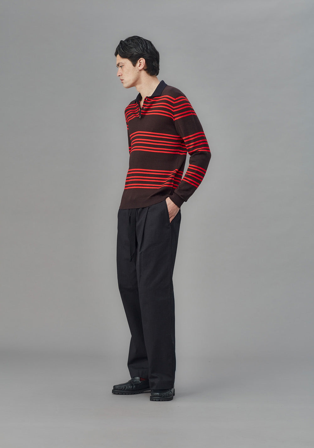 Man wearing a striped sweater and black pants on a gray background