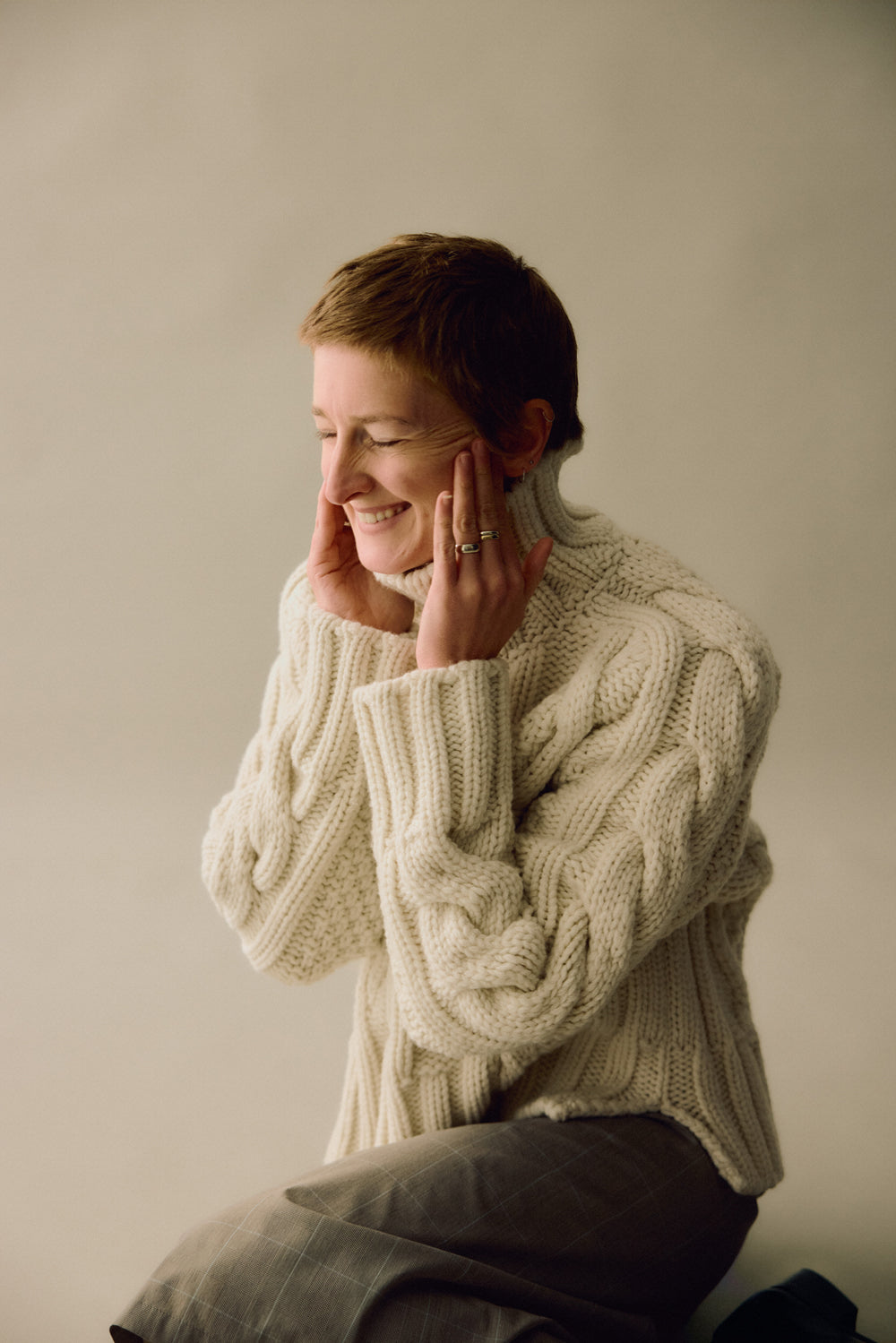 Woman wearing a cream cable knit sweater against a plain background