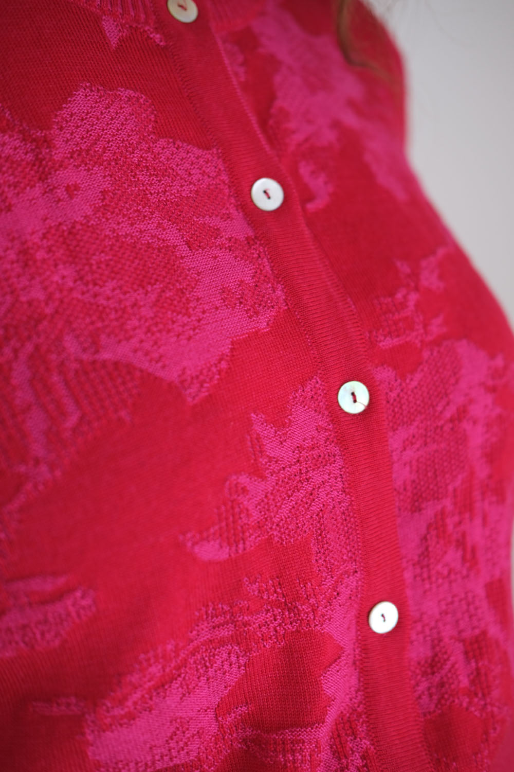 Close-up of a red floral patterned cardigan with buttons on a white background