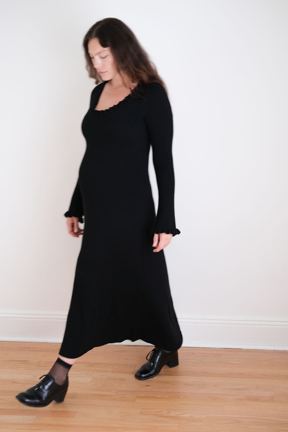 Woman wearing a black dress standing against a white wall.