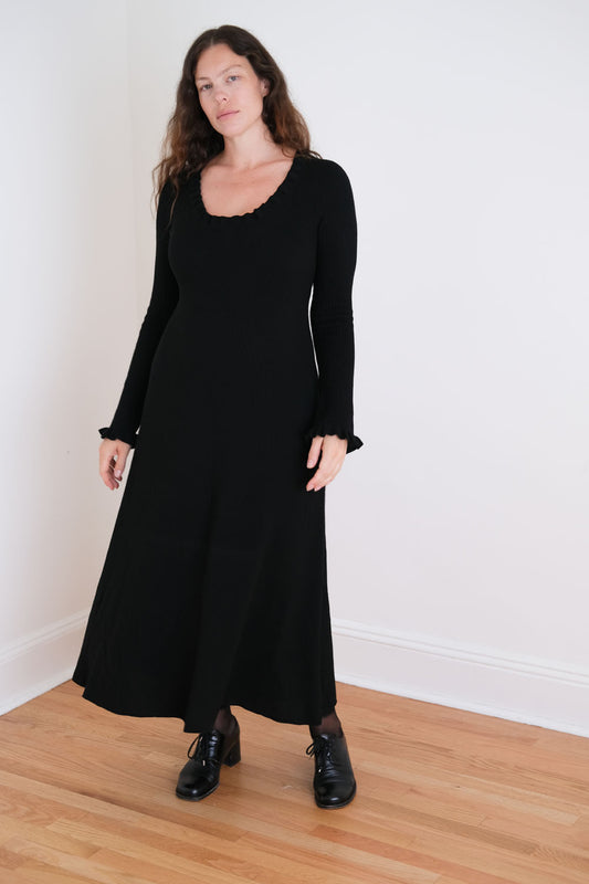 Woman wearing a black dress standing against a white wall.