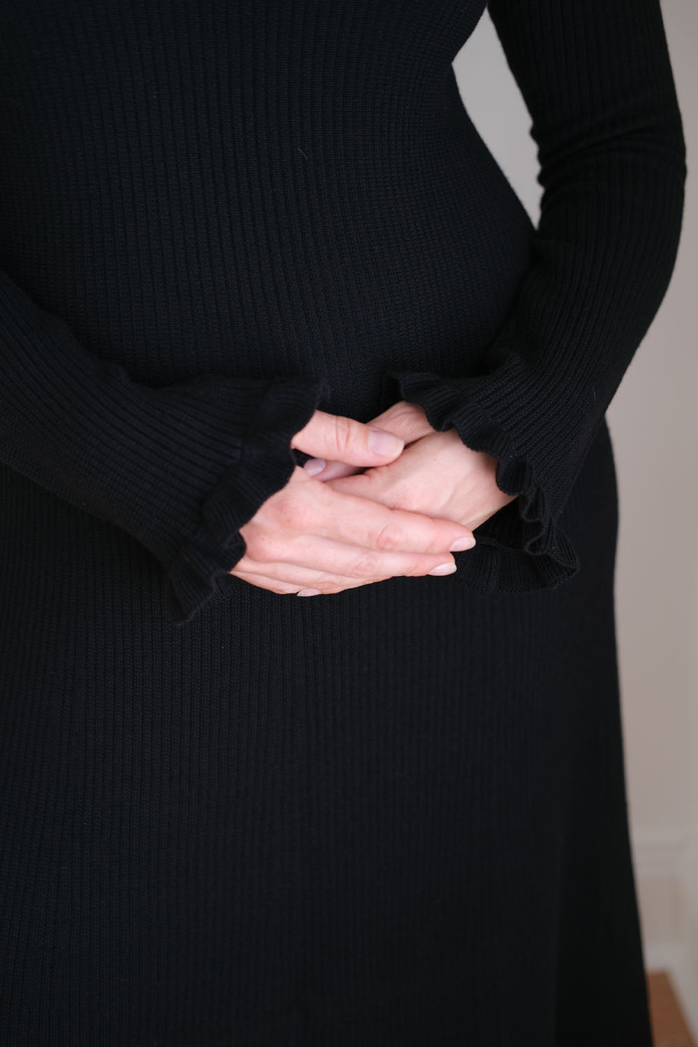 Woman wearing a black dress with hands clasped in front