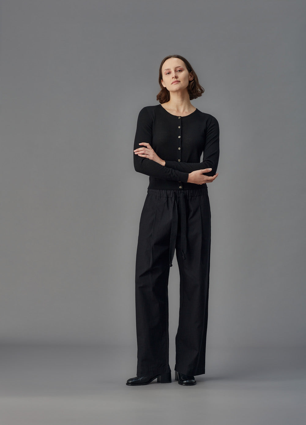 Woman wearing a black merino cardigan against a gray background