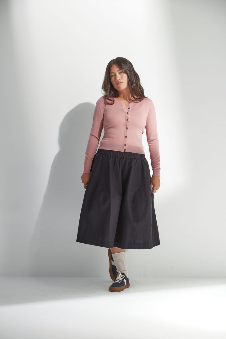 Woman wearing a pink cardigan and black skirt against a white background