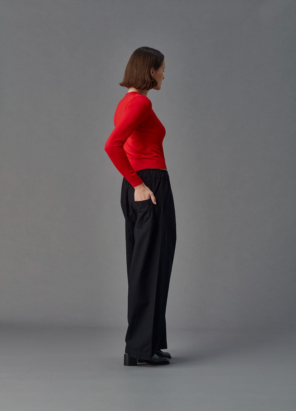 Woman wearing a red merino cardigan against a gray background