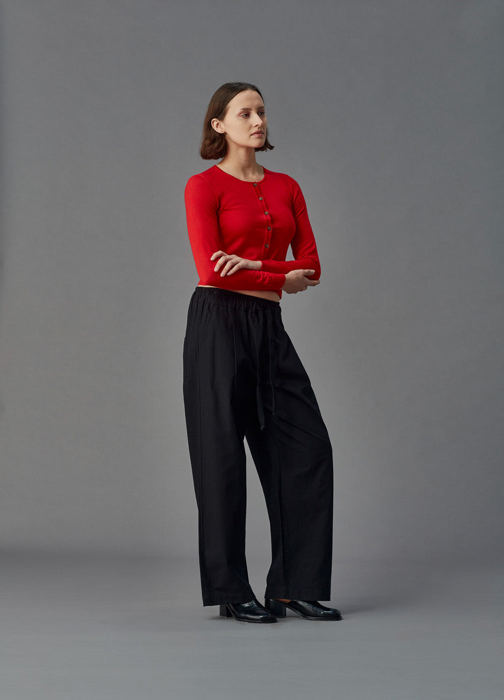Woman wearing a red merino cardigan against a gray background