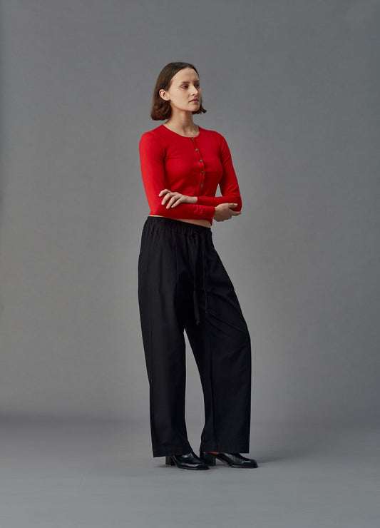 Woman wearing a red merino cardigan against a gray background