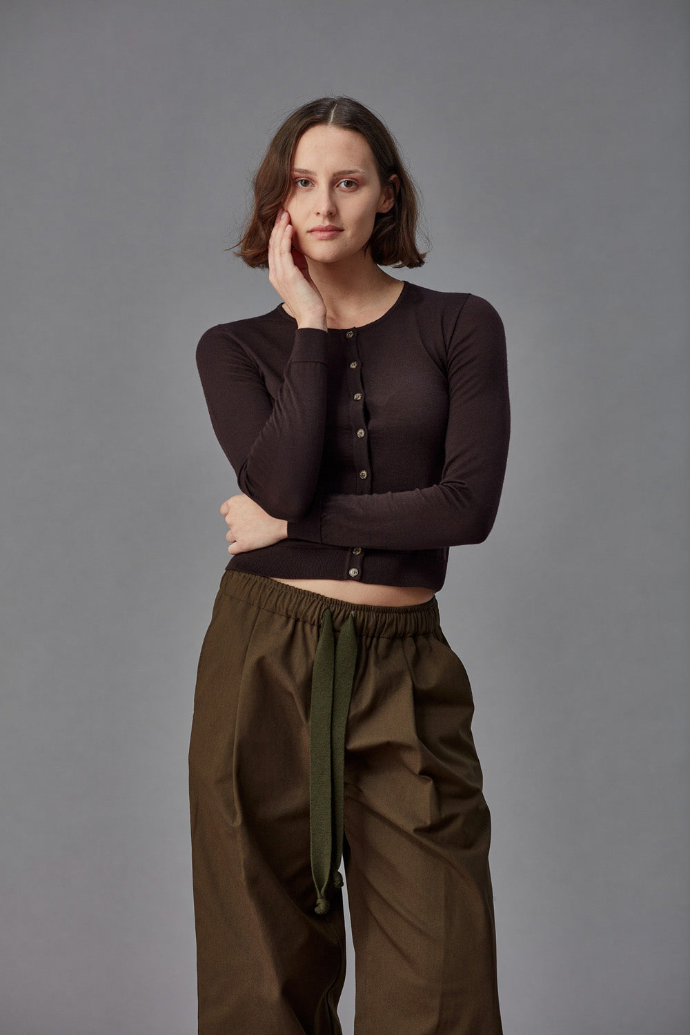 Woman wearing a brown merino cardigan against a gray background