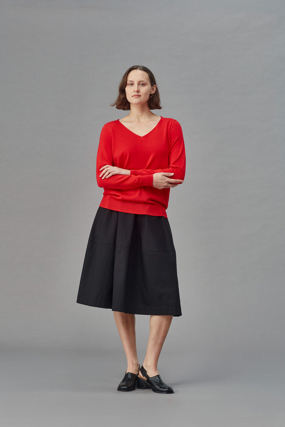 Woman wearing a red slouchy merino sweater and black skirt on a gray background