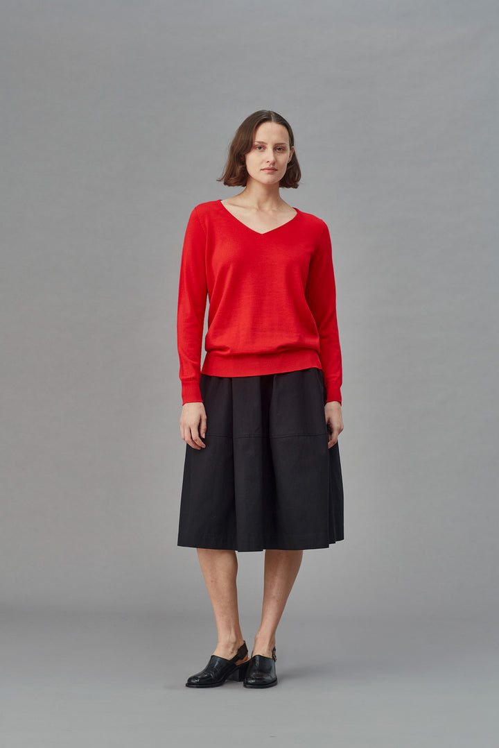 Woman wearing a red slouchy merino sweater and black skirt on a gray background