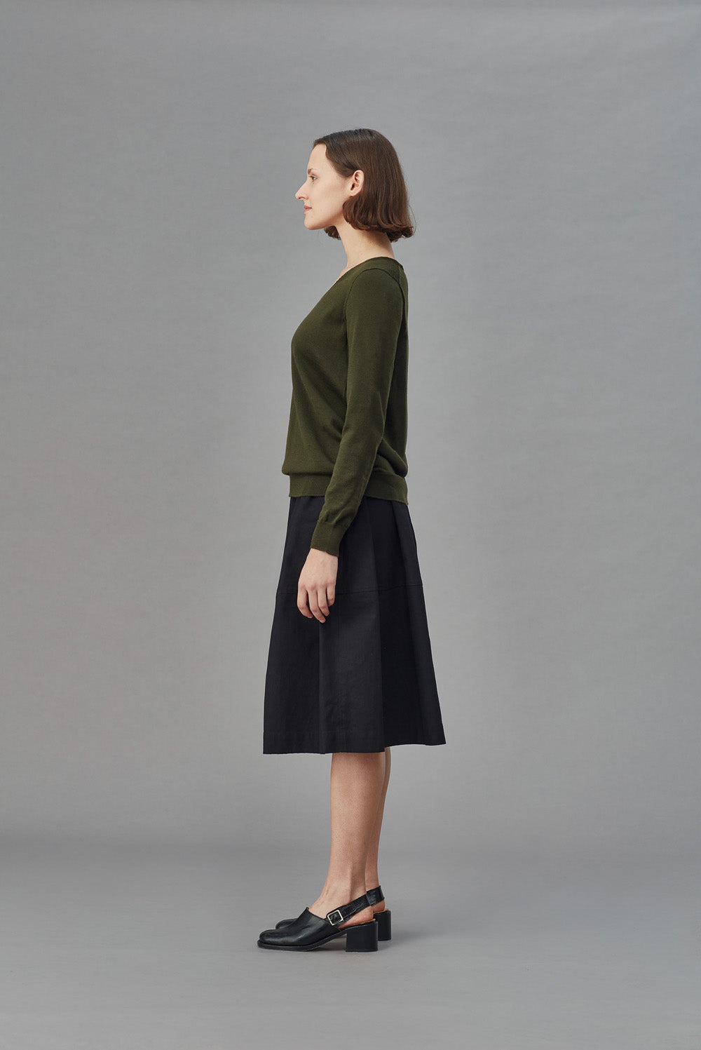 Woman wearing a green merino slouchy sweater and black skirt on a gray background