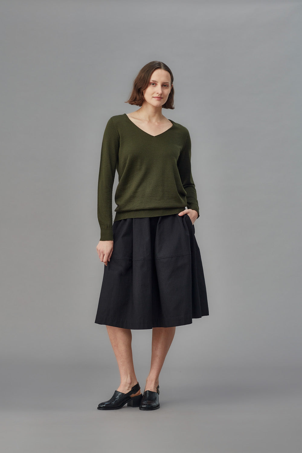 Woman wearing a green merino slouchy sweater and black skirt on a gray background