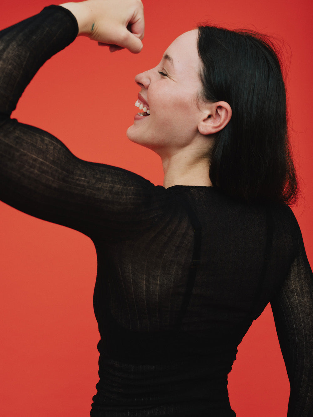 Woman wearing a black sheer tulle top against a red background