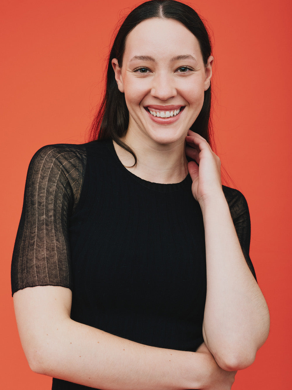 Woman wearing a sheer black tulle top against an orange background