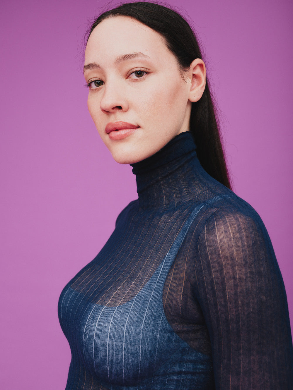 Woman wearing a sheer blue tulle top against a purple background