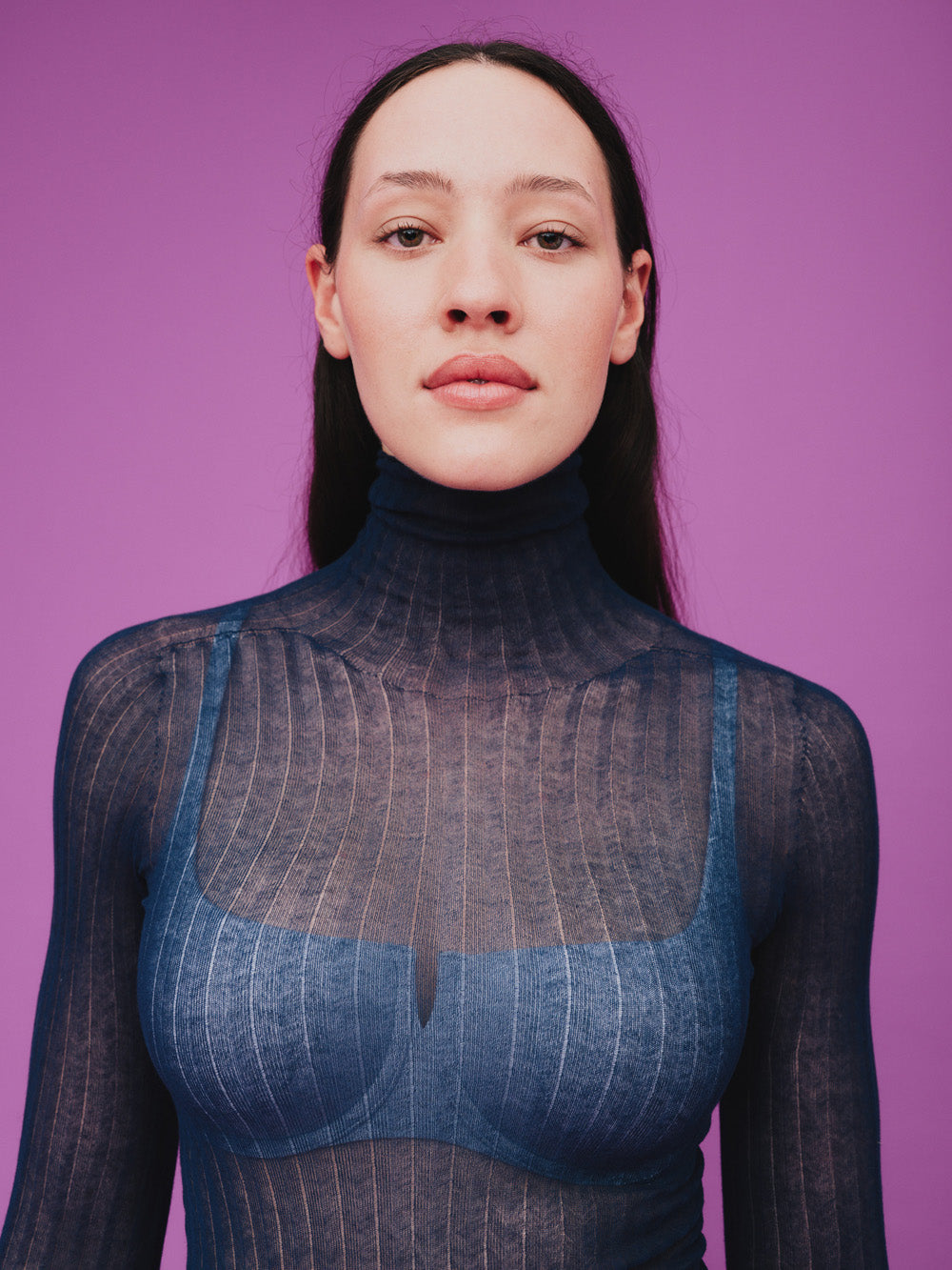 Woman wearing a sheer blue tulle top against a purple background