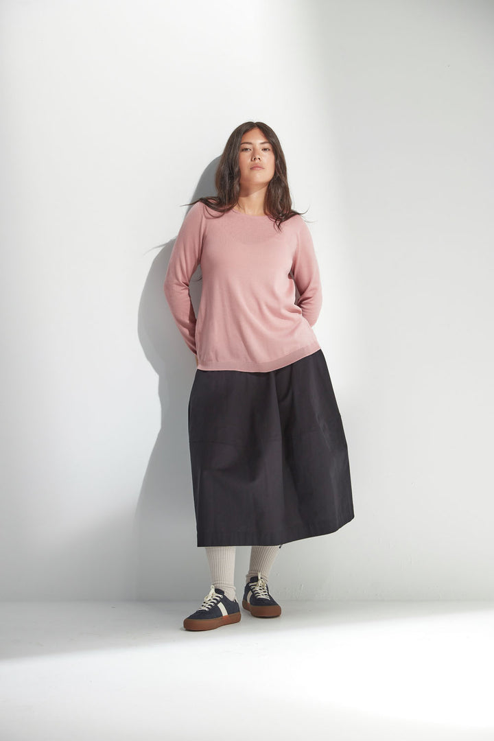 Woman wearing a pink top and black skirt against a white background