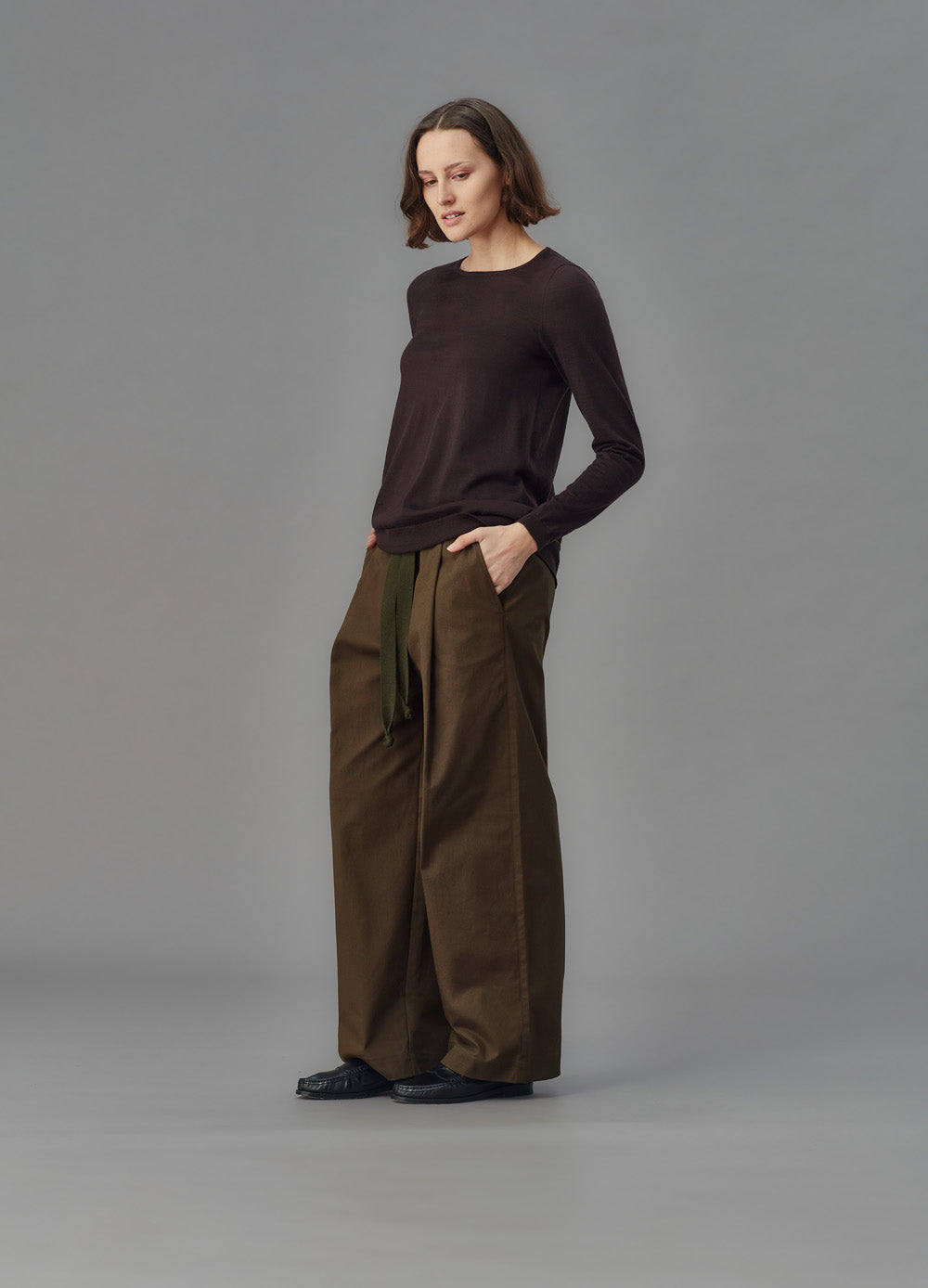 Woman wearing a brown sweater and wide-leg pants against a gray background