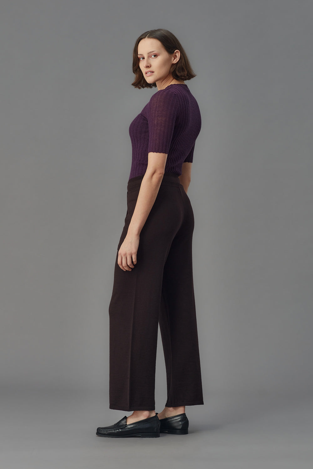 Woman wearing a purple merino ribbed tulle t-shirt and dark pants against a gray background