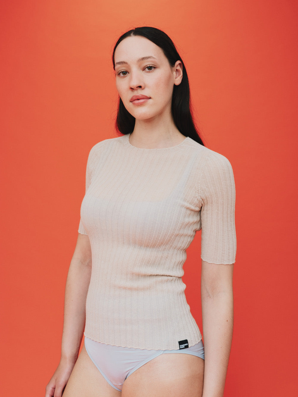 Woman wearing a pearl white merino tulle top against a orange background