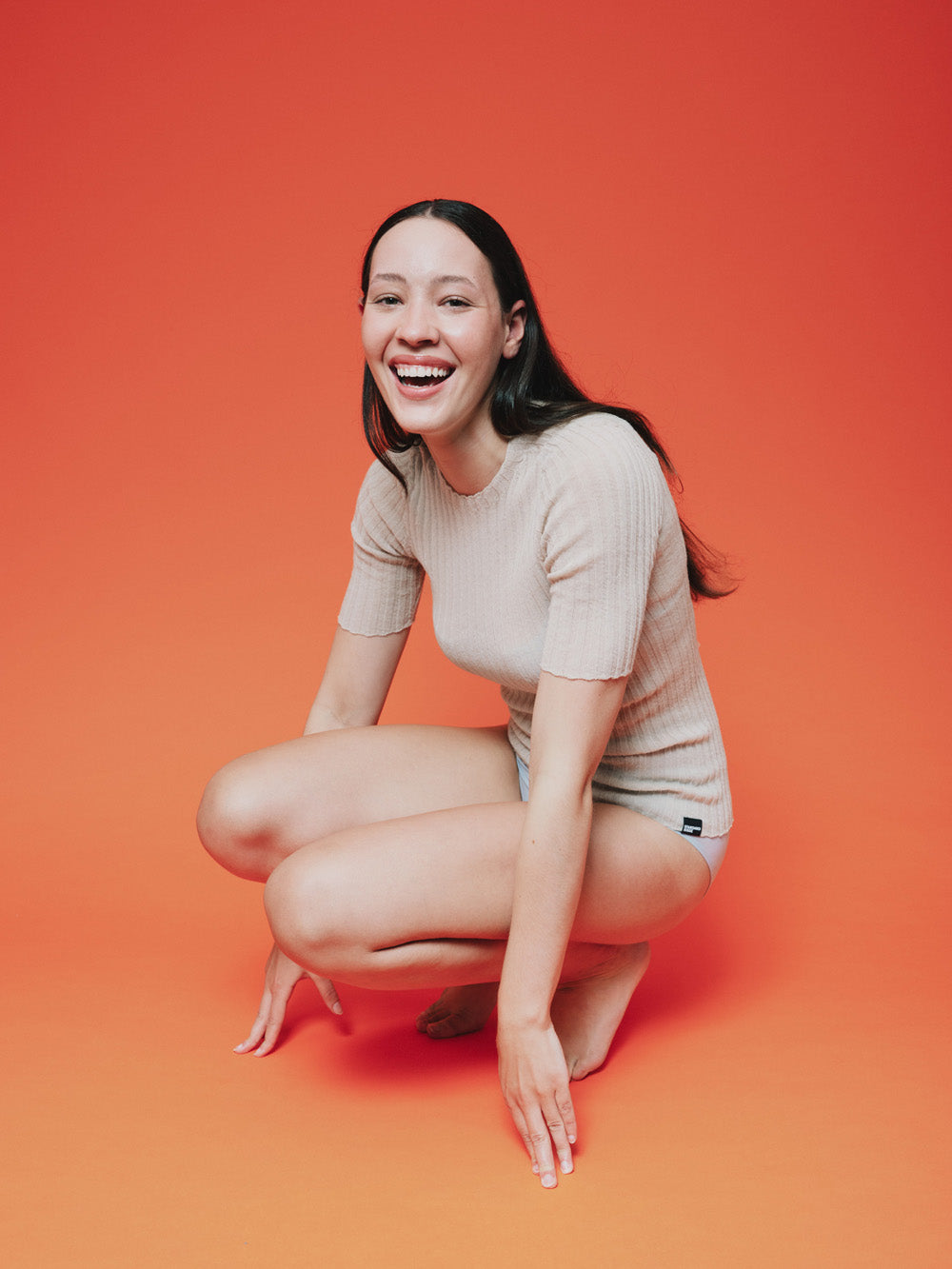 Woman wearing a pearl white merino tulle top against a orange background