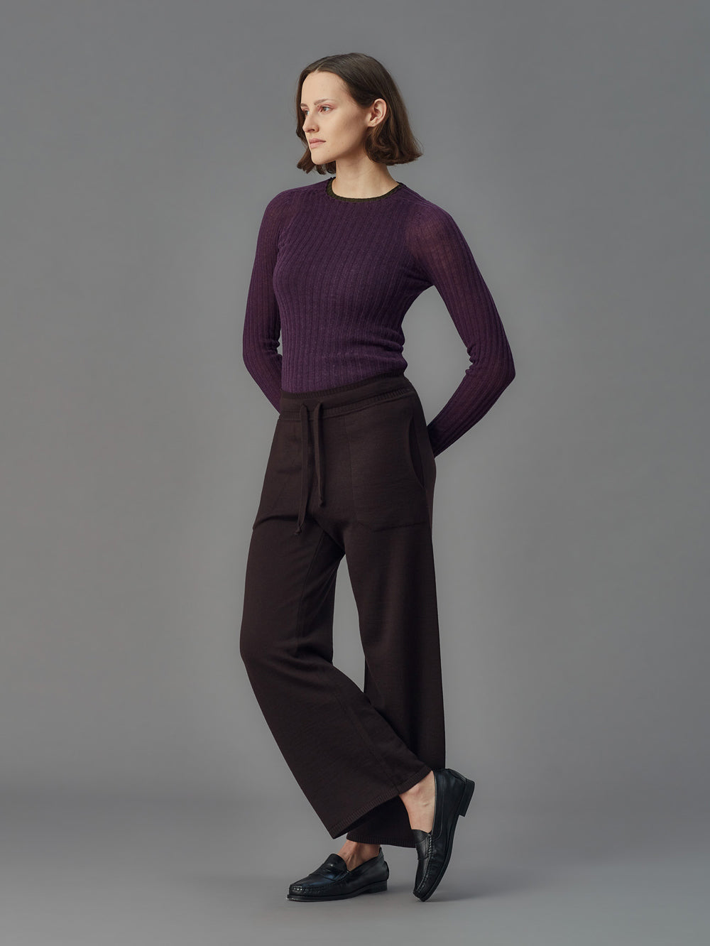 Woman wearing a purple ribbed merino tulle and dark pants on a gray background