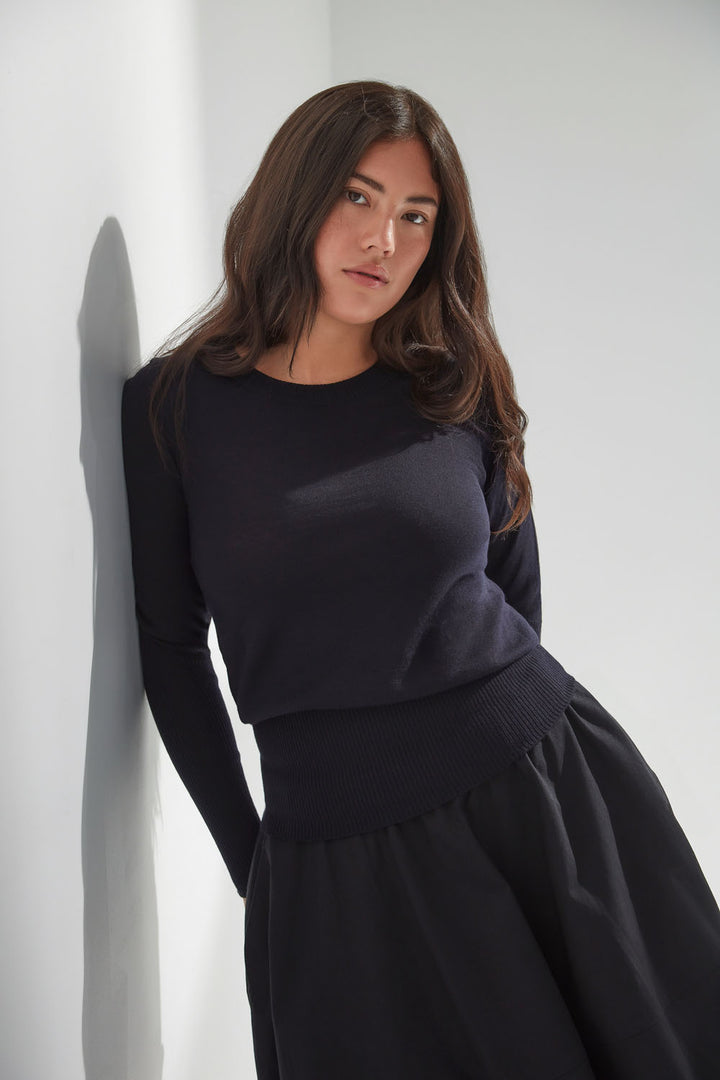 Woman wearing a navy sweater with a black skirt against a white background