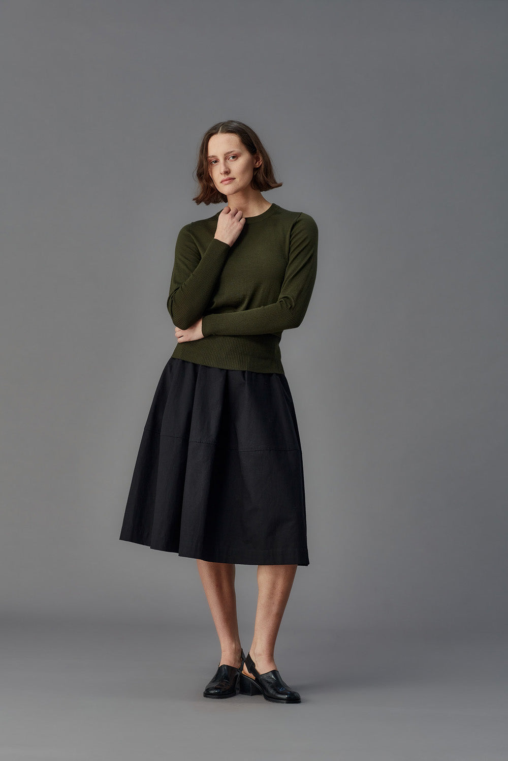 Woman wearing a green sweater and black skirt against a gray background