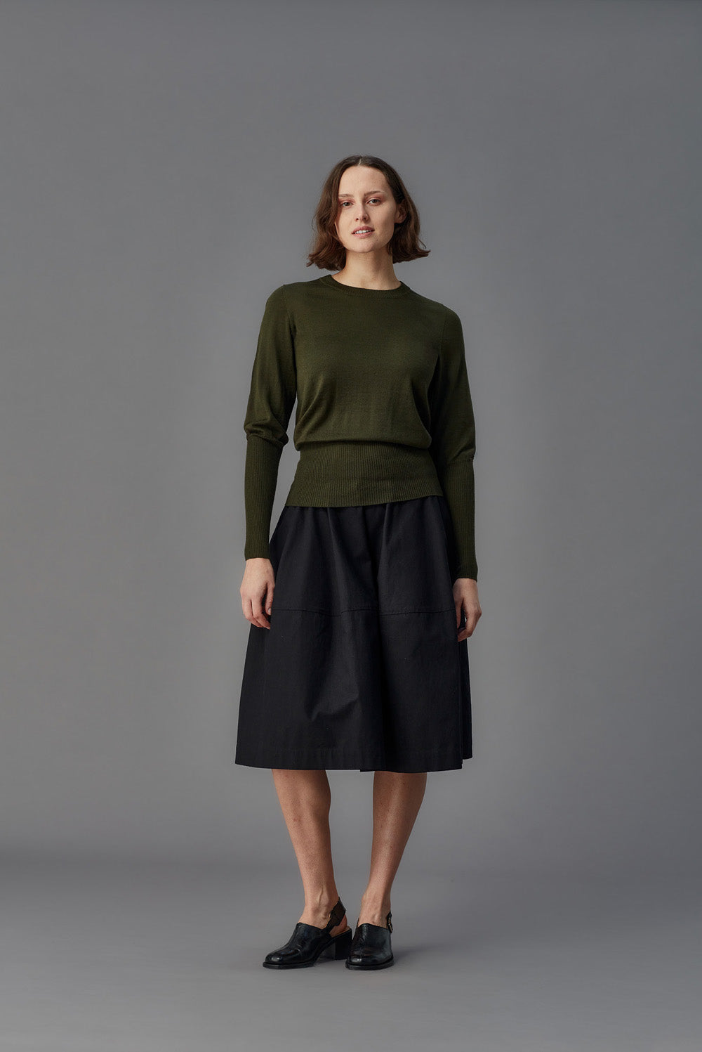 Woman wearing a green sweater and black skirt against a gray background