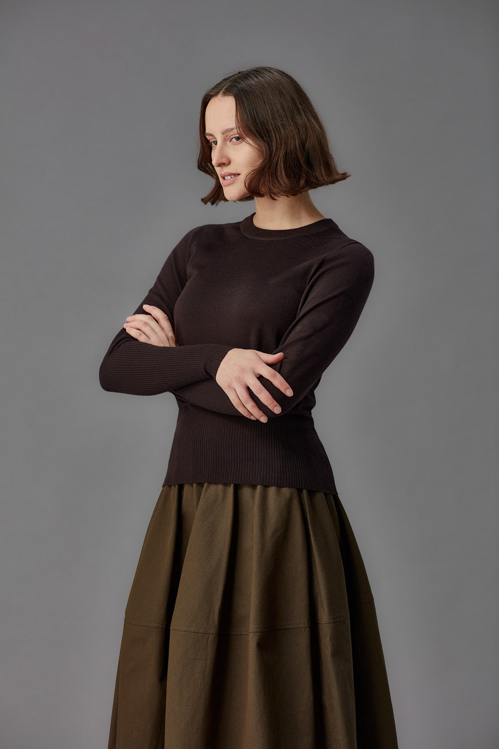 Woman wearing a brown sweater and skirt against a gray background