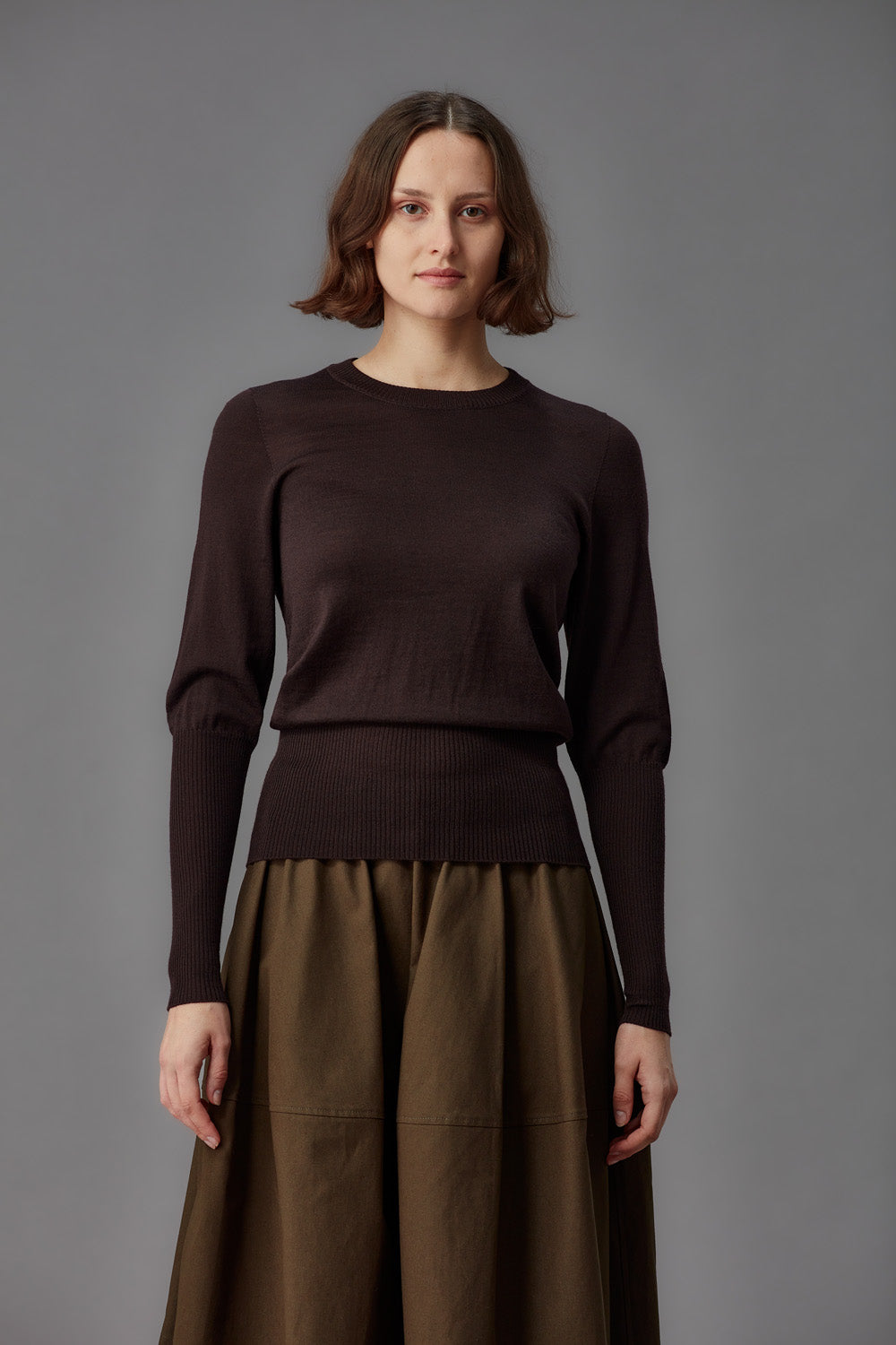 Woman wearing a brown sweater and skirt against a gray background