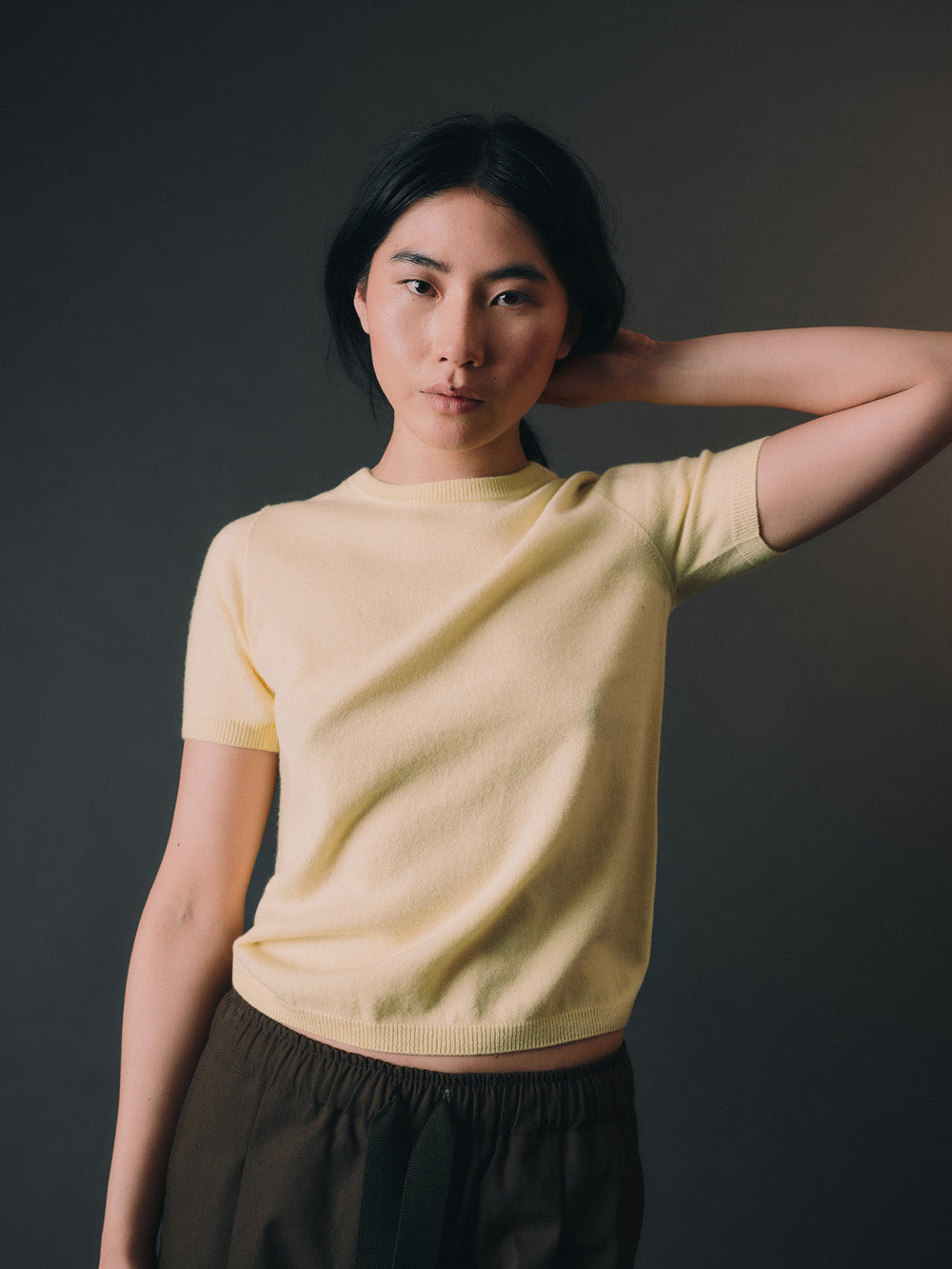 Woman wearing a light yellow cashmere top and dark pants against a dark background