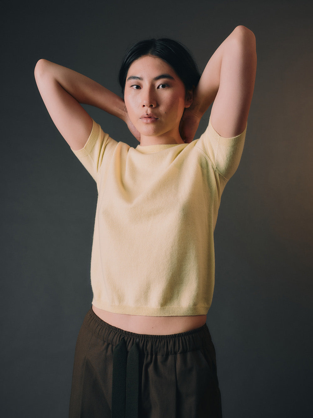 Woman wearing a light yellow cashmere top and dark pants against a dark background