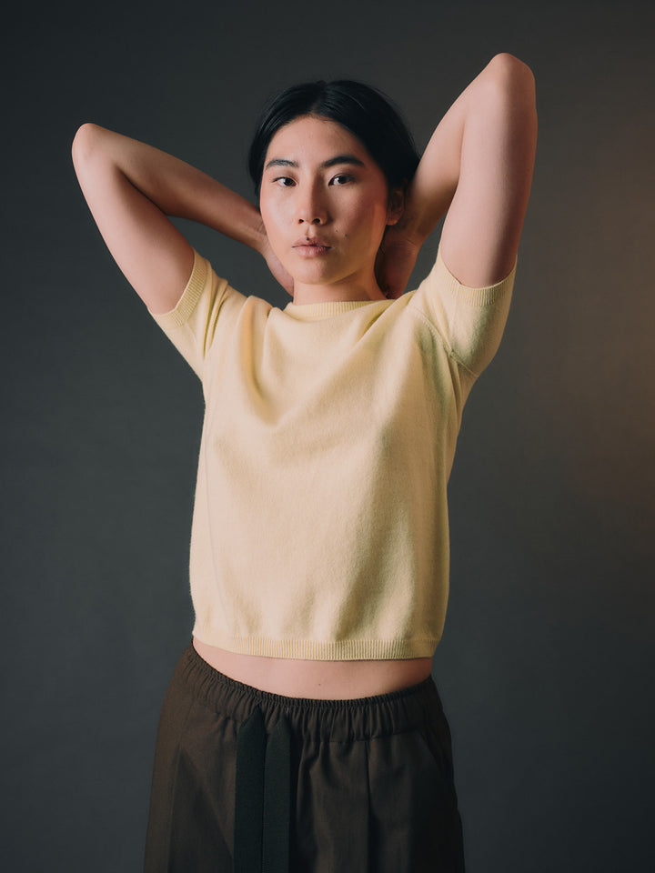 Woman wearing a light yellow cashmere top and dark pants against a dark background