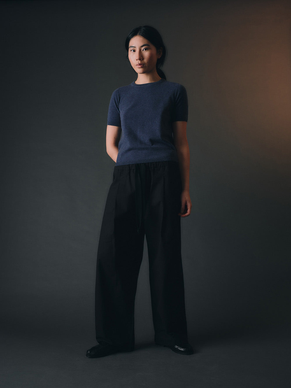 Woman wearing a blue cashmere top and dark pants against a dark background