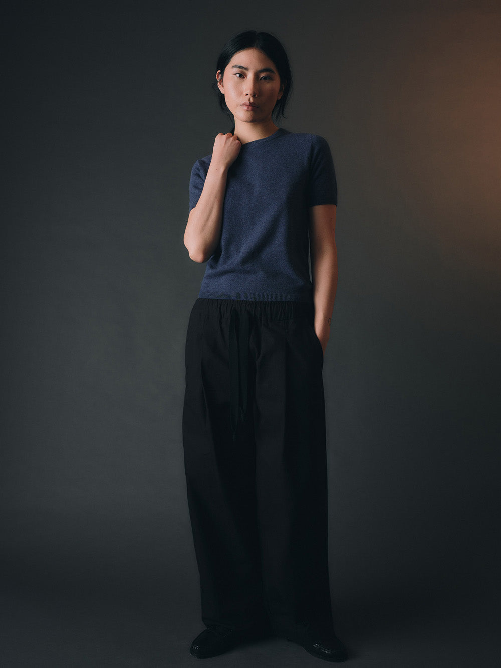 Woman wearing a blue cashmere top and dark pants against a dark background